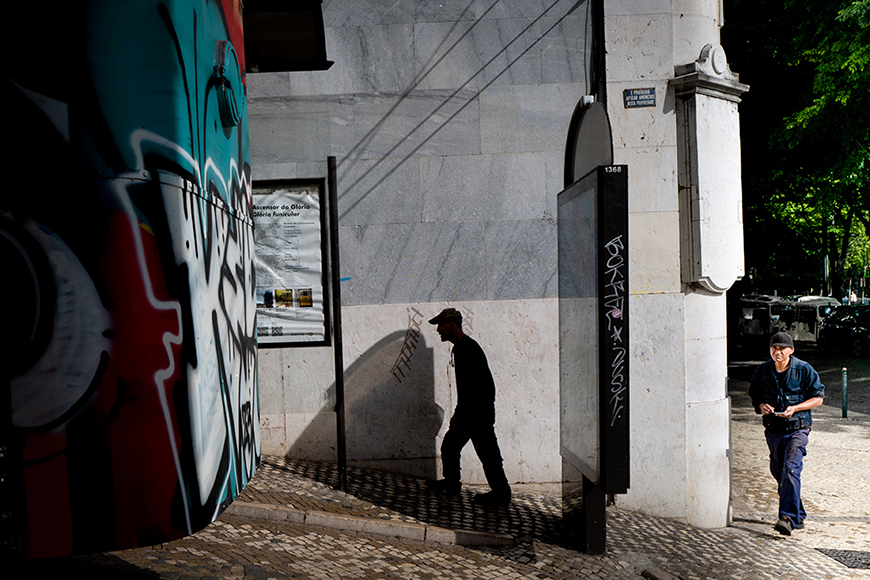 A man walking down a street with graffiti on the wall.