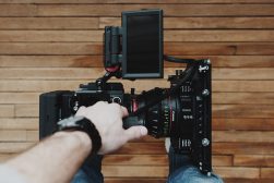 a person holding a camera rig with film camera attached in front of a wooden wall.