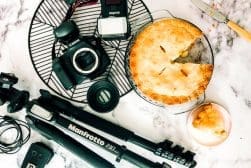 A pie, camera, tripod and other equipment on a marble table.