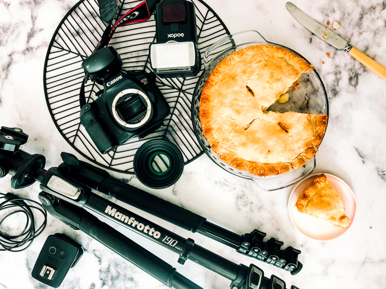 A pie, camera, tripod and other equipment on a marble table.