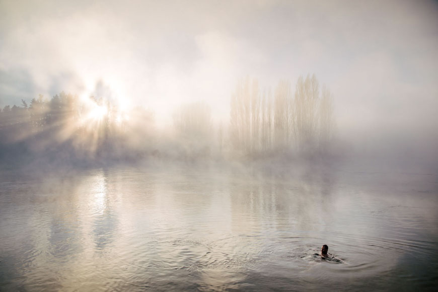 A man is swimming in a river with mist in the background.