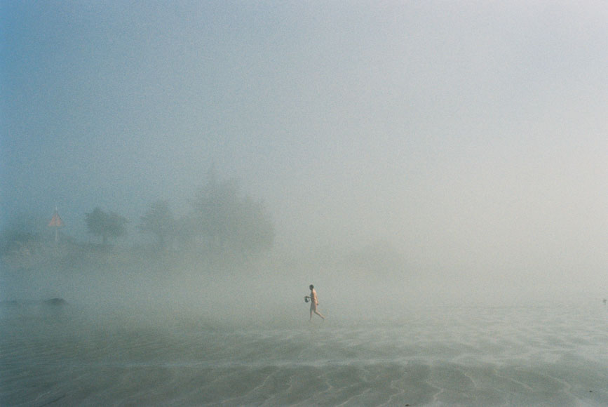 A person walking in the fog on a beach.