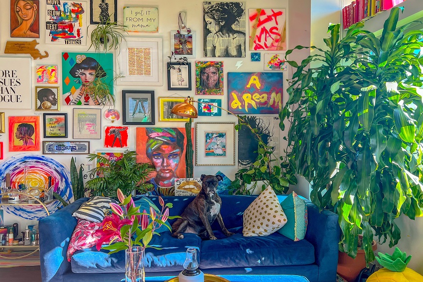 A blue couch in a living room with a lot of art on the wall.