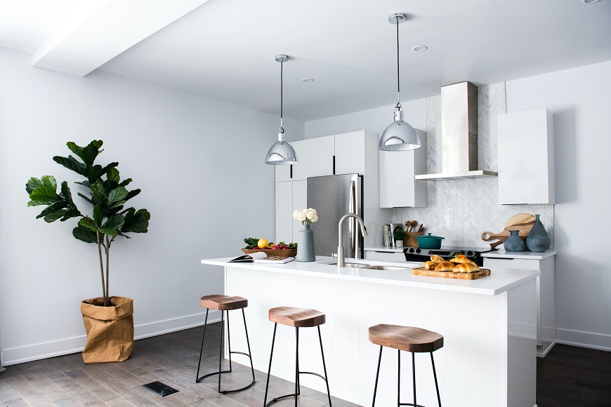 A white kitchen with stools and a plant.