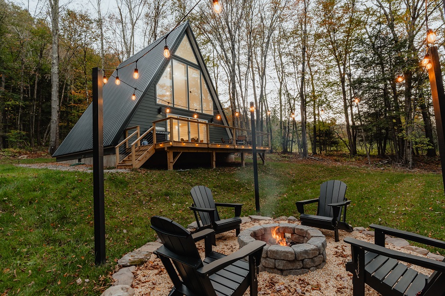 An a-frame cabin with a fire pit in the woods.