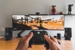A person holding a xbox one controller in front of a monitor.