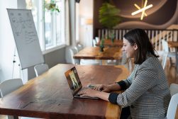 a woman sitting at a well lit table using Zoom on a laptop computer.